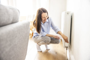A woman adjusts the temperature valve on a radiator.