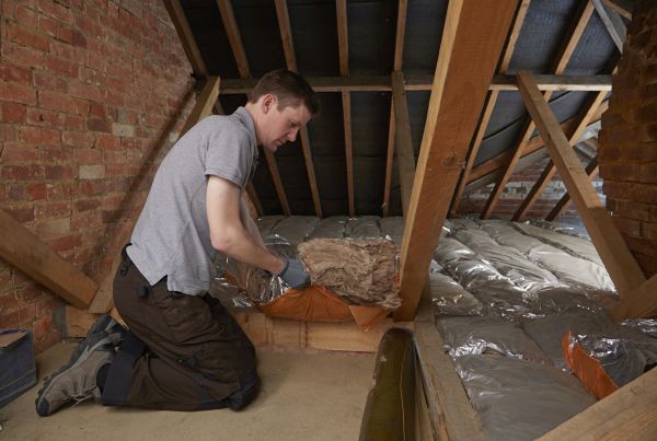 man kneeling in loft space, unpacking loft insulation